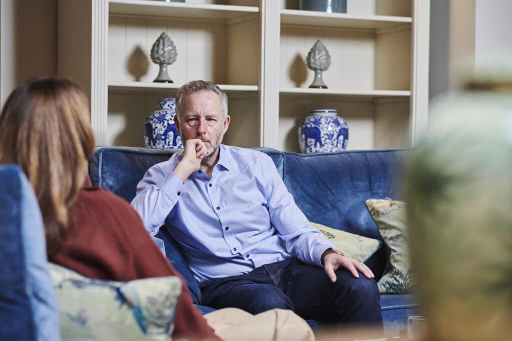 Man in light blue shirt sitting thoughtfully on a blue sofa in living room with decorative vases
